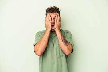 Yeşil arka planda izole edilmiş genç beyaz adam yüzünün yarısını palmiyeyle örterek eğleniyor..