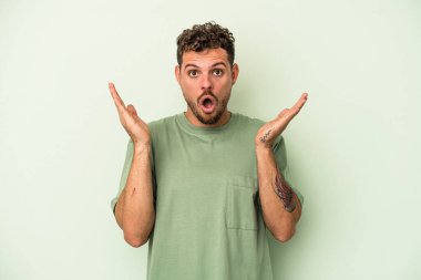 Yeşil arka planda izole genç beyaz adam şaşırdı ve şok oldu..