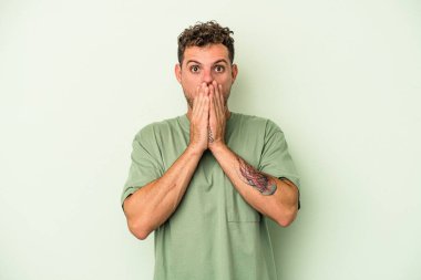 Yeşil arka planda izole edilmiş genç beyaz adam elleriyle ağzını kapatırken şok oldu..