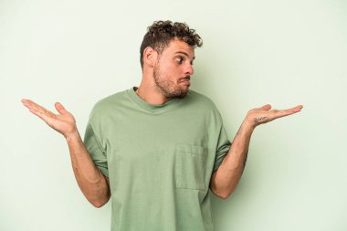 Kafkasyalı genç adam yeşil arka planda izole edilmiş. Kafası karışmış ve omuz silkiyor. Kopya alanını tutmak için..