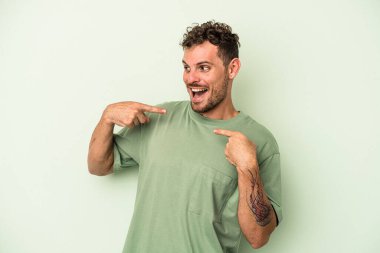 Yeşil arka planda izole edilmiş genç beyaz adam parmağını göstererek şaşırdı, geniş bir gülümsemeyle..