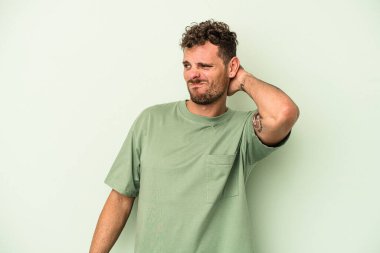 Yeşil arka planda izole edilmiş genç beyaz adam yorgun ve uykulu, elini başının üstünde tutuyor..