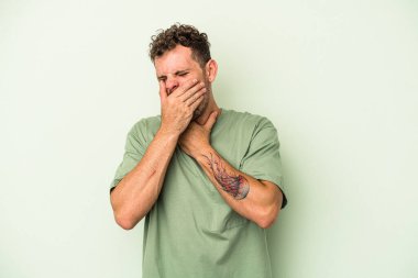 Yeşil arka planda izole edilmiş genç beyaz bir adam virüs veya enfeksiyon yüzünden boğazında ağrı hissediyor..