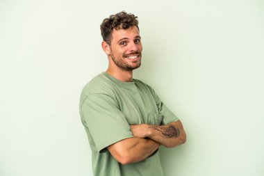 Yeşil arka planda kendini güvende hisseden, kararlı kollarını kavuşturan genç beyaz bir adam..