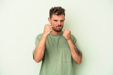 Yeşil arka planda izole edilmiş genç beyaz adam yumruğunu kameraya gösteriyor, agresif yüz ifadesi var..