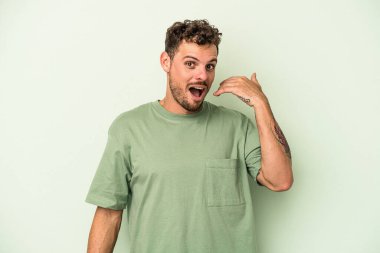 Yeşil arka planda izole edilmiş genç beyaz bir adam bir şeye gülüyor, elleriyle ağzını kapatıyor..