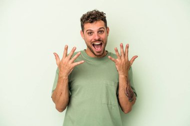 Yeşil arka planda izole edilmiş genç beyaz adam on numarayı elleriyle gösteriyor..