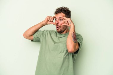 Yeşil arka planda izole edilmiş genç beyaz adam bir başarı fırsatı bulmak için gözlerini açık tutuyor..