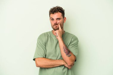 Kafkasyalı genç adam yeşil arka planda izole edilmiş. Mutsuz, iğneleyici bir ifadeyle kameraya bakıyor..