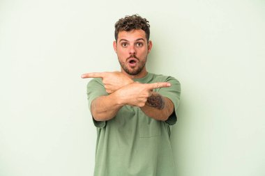 Yeşil arka plan noktalarında izole genç beyaz adam, iki seçenek arasında seçim yapmaya çalışıyor.