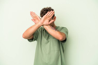 Yeşil arka planda izole genç beyaz adam iki kolu çapraz tutuyor, inkar kavramı.