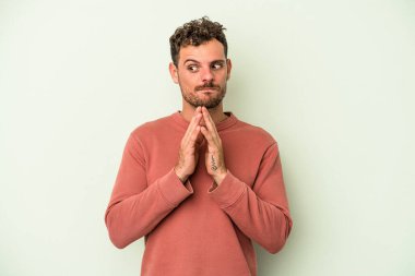 Kafkasyalı genç adam yeşil arka planda izole edilmiş dua ediyor, bağlılık gösteriyor, dindar biri ilahi ilham arıyor..