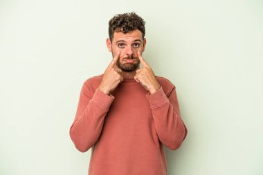 Kafkasyalı genç adam yeşil arka planda izole edilmiş, ağlıyor, bir şeyden memnun değil, acı ve kafa karışıklığı kavramı..