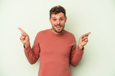 Yeşil arka planda izole edilmiş genç beyaz adam farklı kopya alanlarını gösteriyor, birini seçiyor, parmaklarıyla gösteriyor.