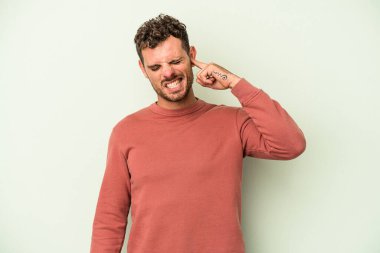 Genç beyaz adam yeşil arka planda izole edilmiş parmaklarıyla kulaklarını kapatan, yüksek sesli bir ortam tarafından stresli ve umutsuz..