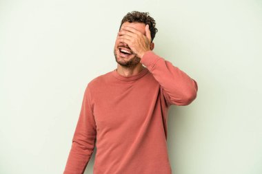 Yeşil arka planda izole edilmiş genç beyaz adam elleriyle gözlerini kapatıyor, geniş bir gülümsemeyle bir sürpriz bekliyor..