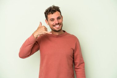 Yeşil arka planda izole edilmiş genç beyaz adam parmaklarıyla bir cep telefonu hareketi gösteriyor..
