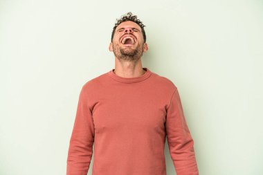 Genç beyaz adam yeşil arka planda izole edilmiş rahat ve mutlu bir şekilde gülüyor, boynunda dişlerini gösteriyor..