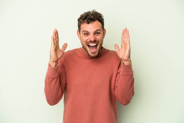 Yeşil arka planda izole genç beyaz adam hoş bir sürpriz alıyor, heyecanlı ve el kaldırıyor..