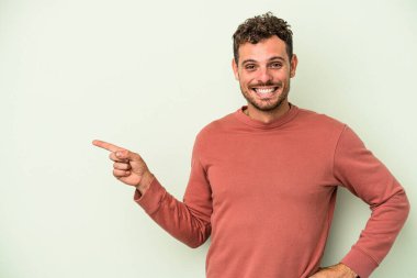 Yeşil arka planda izole edilmiş genç beyaz adam işaret parmağıyla işaret ederek gülümsüyor..