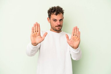 Yeşil arka planda izole edilmiş genç beyaz adam elini uzatmış, dur işareti göstererek seni engelliyor..