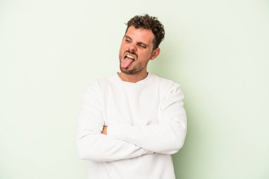 Genç beyaz adam yeşil arka planda izole edilmiş komik ve dost canlısı bir dil uzatıyor..