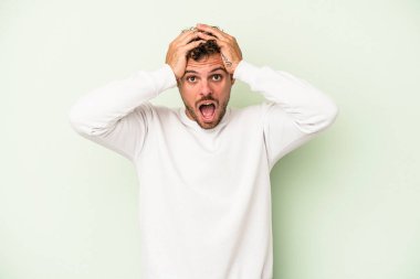 Yeşil arka planda izole genç beyaz adam şaşırdı ve şok oldu..