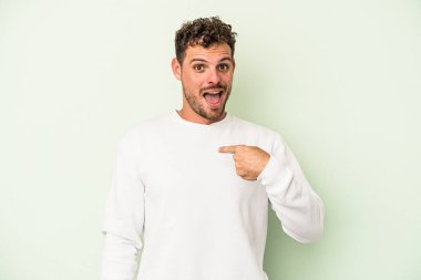 Yeşil arka planda izole edilmiş genç beyaz adam parmağını göstererek şaşırdı, geniş bir gülümsemeyle..
