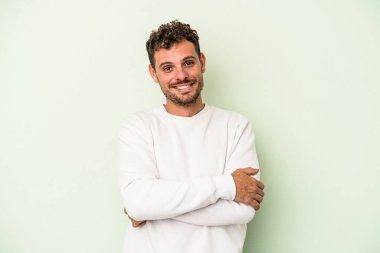 Yeşil arka planda kendini güvende hisseden, kararlı kollarını kavuşturan genç beyaz bir adam..