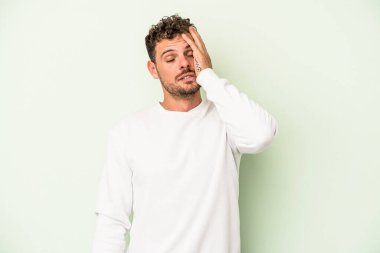 Yeşil arka planda izole edilmiş genç beyaz adam yorgun ve uykulu, elini başının üstünde tutuyor..