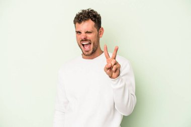 Yeşil arka planda izole edilmiş genç beyaz adam iki numarayı parmaklarıyla gösteriyor..