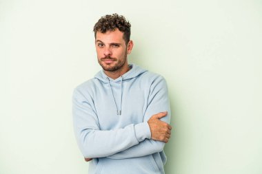 Kafkasyalı genç adam yeşil arka planda izole edilmiş. Mutsuz, iğneleyici bir ifadeyle kameraya bakıyor..