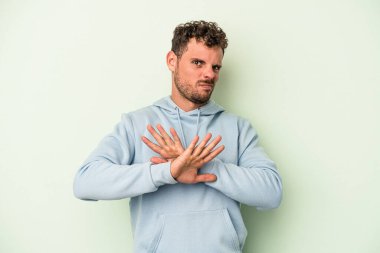 Genç beyaz adam yeşil arka planda izole edilmiş bir şekilde inkar jesti yapıyor.