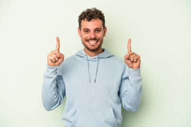 Yeşil arka planda izole genç beyaz adam işaret iki ön parmakları boş bir boşluk gösteren.