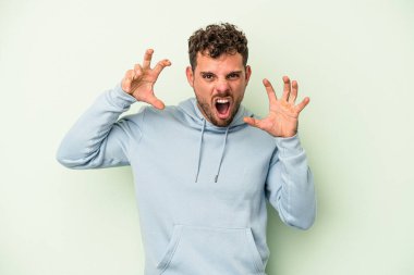 Yeşil arka planda izole edilmiş genç beyaz adam pençelerini kedi taklidi yaparken gösteriyor, agresif bir hareket..