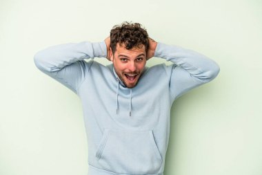 Genç beyaz adam yeşil arka planda izole edilmiş bağırıyor, çok heyecanlı, tutkulu, bir şeyden memnun..