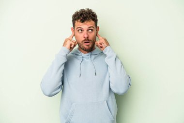 Genç beyaz adam yeşil arka planda izole edilmiş parmaklarıyla kulaklarını kapatan, yüksek sesli bir ortam tarafından stresli ve umutsuz..