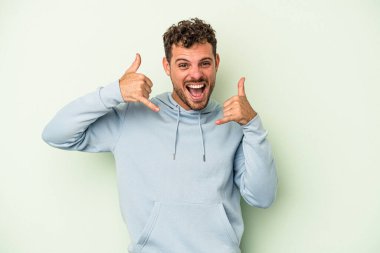 Yeşil arka planda izole edilmiş genç beyaz adam parmaklarıyla bir cep telefonu hareketi gösteriyor..