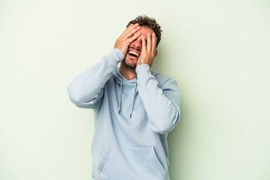 Yeşil arka planda izole edilmiş genç beyaz adam ellerini başının üstünde tutarak neşe içinde gülüyor. Mutluluk kavramı.