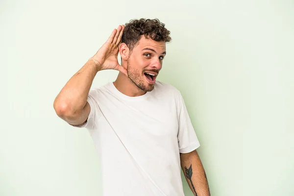 Jovem Caucasiano Isolado Fundo Verde Tentando Ouvir Uma Fofoca — Fotografia de Stock