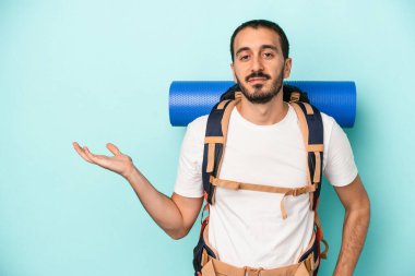 Mavi arka planda izole edilmiş beyaz tenli genç bir adam bir palmiye üzerinde fotokopi alanı ve belinde bir el daha gösteriyor..