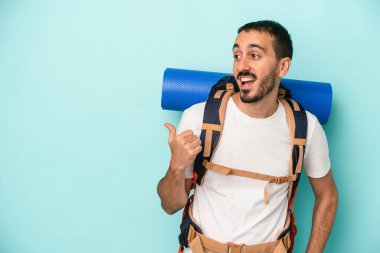 Kafkasyalı genç yürüyüşçü mavi arka planda izole edilmiş başparmak uzakta, gülüyor ve kaygısız.