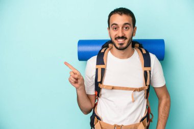 Beyaz tenli genç adam mavi arka planda izole edilmiş gülümsüyor ve boş alanda bir şeyler gösteriyor..