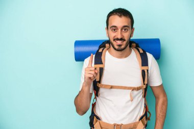 Genç beyaz yürüyüşçü, mavi arka planda izole edilmiş. Bir numarayı parmağıyla gösteriyor..