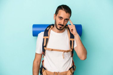 Kafkasyalı genç yürüyüşçü mavi arka planda izole edildi. Şakağı parmağıyla göstererek, düşünerek, bir göreve odaklandı..