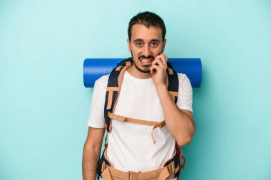 Genç beyaz yürüyüşçü, mavi arka planda izole edilmiş tırnak yiyor, gergin ve endişeli..