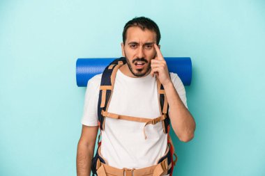 Mavi arka planda izole genç beyaz yürüyüşçü işaret parmağıyla hayal kırıklığı jesti gösteriyor.