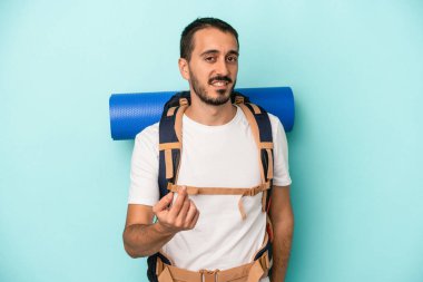 Kafkasyalı genç yürüyüşçü, mavi arka planda izole edilmiş ve sanki seni davet ediyormuş gibi parmağıyla işaret ediyor..