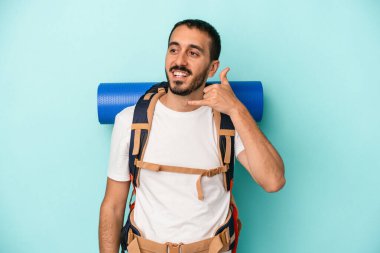 Mavi arka planda izole edilmiş genç beyaz adam parmaklarıyla bir cep telefonu çağrısı hareketi gösteriyor..