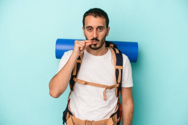 Genç beyaz yürüyüşçü, mavi arka planda izole edilmiş, parmakları dudaklarında bir sır saklıyor..